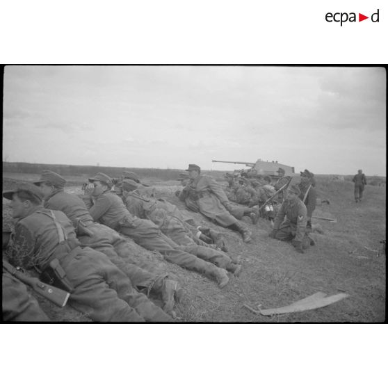Un Nashorn du schwere Panzer Abteilung 519 tire, protégés par un talus des fantassins et des Panzergrenadier observent l'horizon aux jumelles.