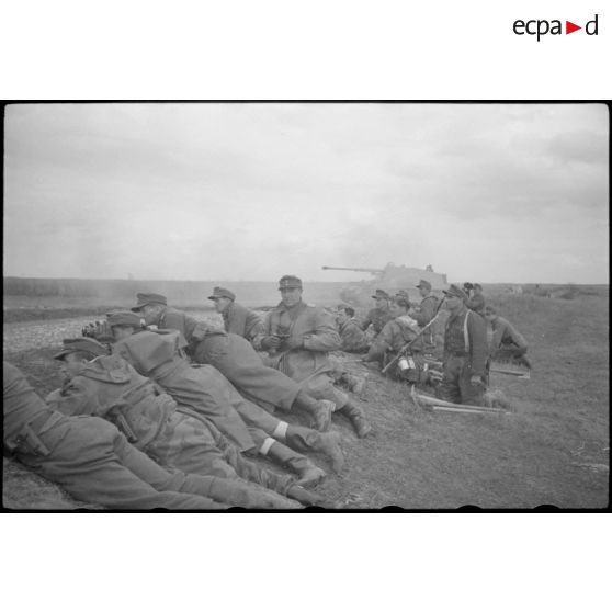 Un Nashorn du schwere Panzer Abteilung 519 tire, protégés par un talus des fantassins et des Panzergrenadier observent l'horizon aux jumelles.