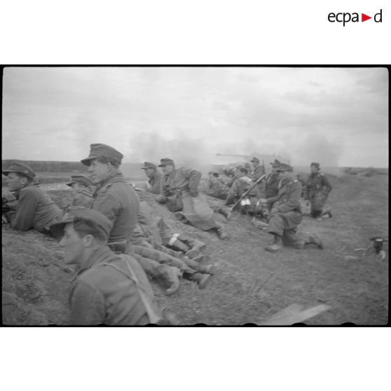 Un Nashorn du schwere Panzer Abteilung 519 tire, protégés par un talus des fantassins et des Panzergrenadier observent l'horizon aux jumelles.