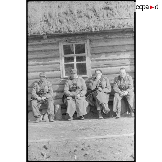 Un sous-officier et trois officiers marquent une pause devant une isba.