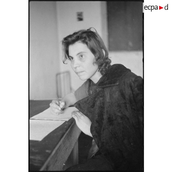 Portrait d'une femme répondant à des questions et rédigeant un courrier, il pourrait s'agir d'un interrogatoire.