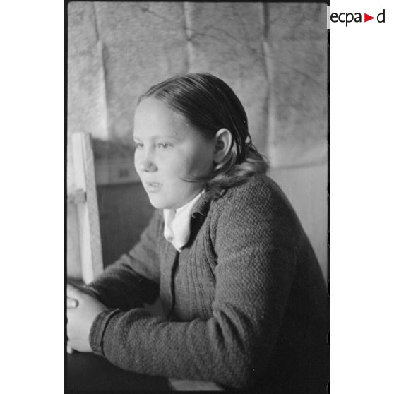 Portrait d'une jeune femme répondant à des questions, une carte est accrochée sur le mur.