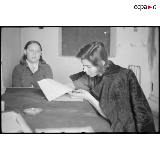 Portrait d'une femme répondant à des questions et rédigeant un courrier, il pourrait s'agir d'un interrogatoire.