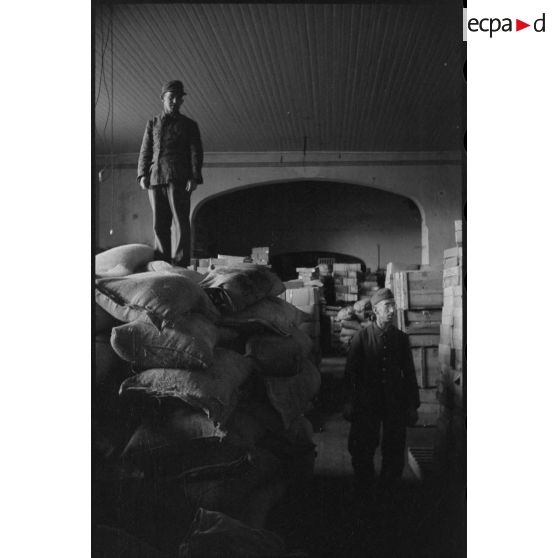 Au sein d'un magasin d'approvisionnement, des soldats entassent des sacs de farine.