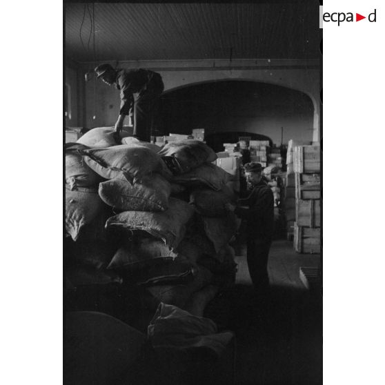 Au sein d'un magasin d'approvisionnement, des soldats entassent des sacs de farine.