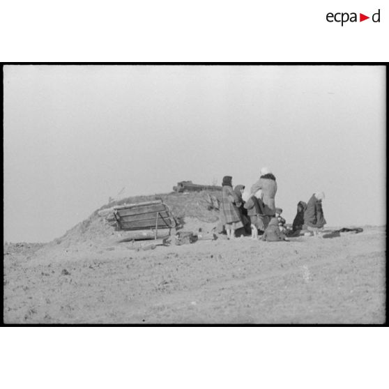 En raison des combats qui se déroulent à proximité, une femme et des enfants se tiennent à proximité d'un abri creusé dans le sol.