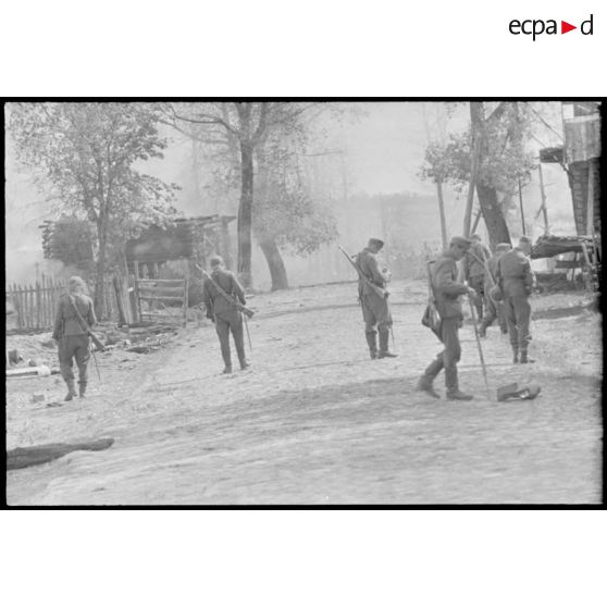 Dans la rue d'un village désert, des fantassins sont à la recherche de mines.