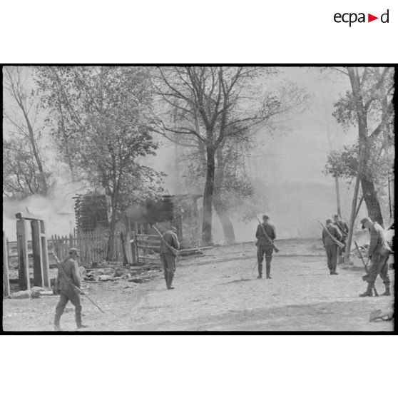 Dans la rue d'un village désert, des fantassins sont à la recherche de mines.