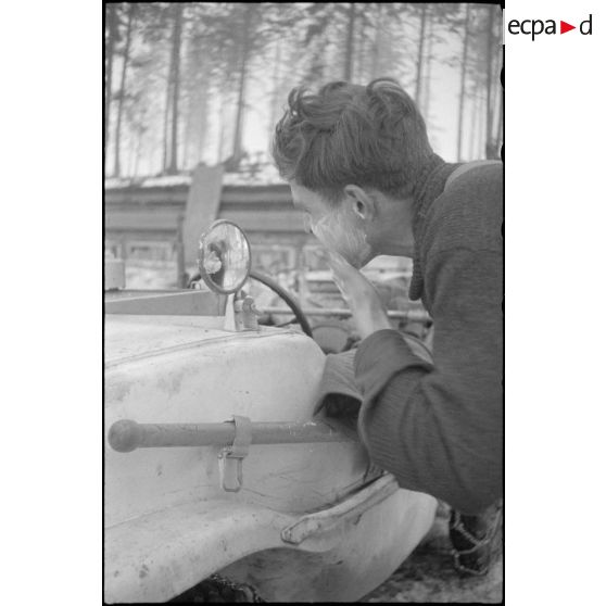 Un fantassin se rase en s'aidant d'un rétroviseur d'un véhicule amphibie Schwimmwagen.