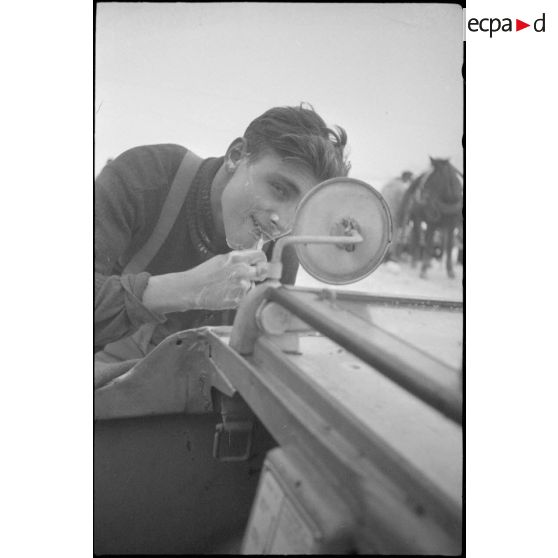 Un fantassins se rase en s'aidant d'un rétro-viseur d'un véhicule amphibie Schwimmwagen.