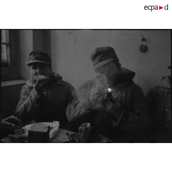 Des fantassins terminent un repas à l'abri d'une maison.