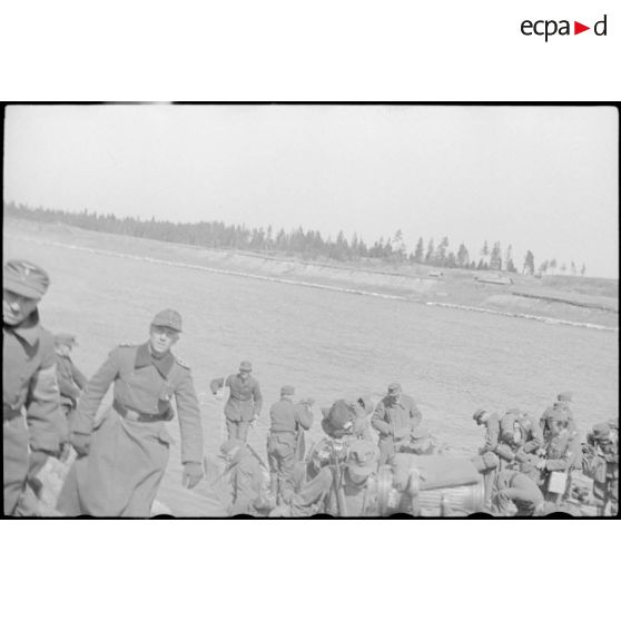 Après la traversée d'une rivière sur un ponton (Brückengerät), le personnel gagne la berge, tandis que des sacs postaux vont être déchargés.
