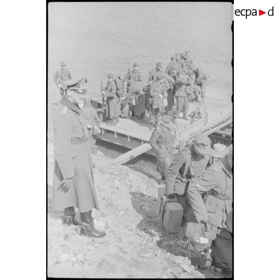 Après la traversée d'une rivière sur un ponton (Brückengerät), le personnel gagne la berge, tandis que des sacs postaux vont être déchargés.