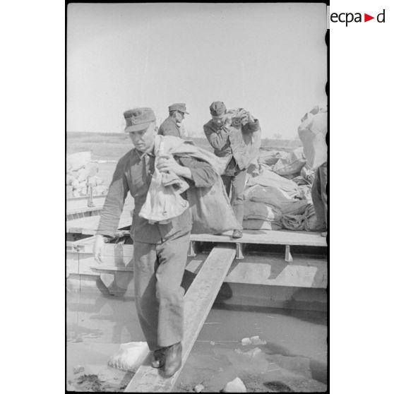 Après la traversée d'une rivière sur un ponton (Brückengerät), des sacs postaux sont déchargés.