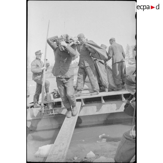 Après la traversée d'une rivière sur un ponton (Brückengerät), des sacs postaux sont déchargés.