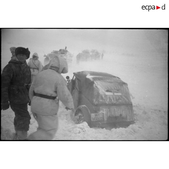 Une Kübelwagen immatriculée WH-1432 613 tente de reprendre la route, des semi-chenillés attentent de passer le pont.