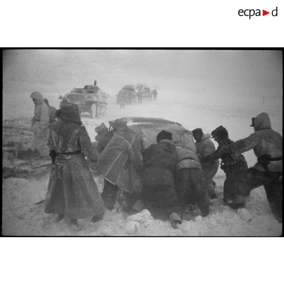 Une Kübelwagen immatriculée WH-1432 613 tente de reprendre la route, des semi-chenillés attentent de passer le pont.