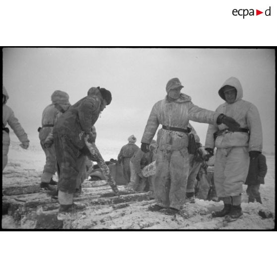 Une Kübelwagen immatriculée WH-1432 613 tente de reprendre la route, des semi-chenillés attentent de passer le pont.