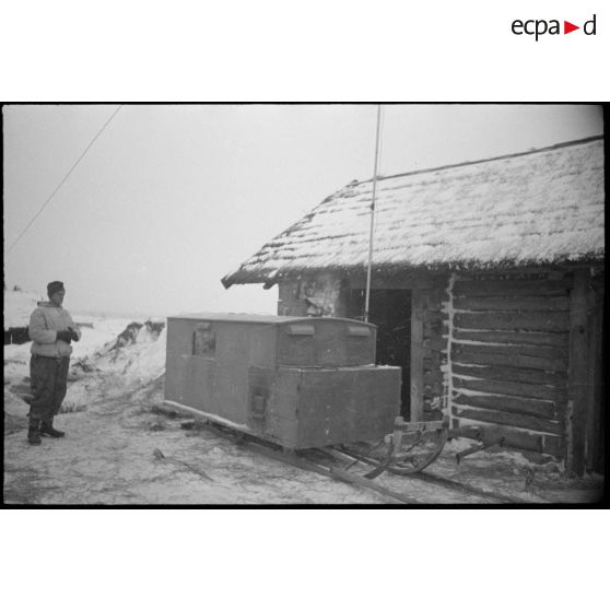 A proximité d'une isba, le reporter photographie un poste émetteur installé sur un traîneau.