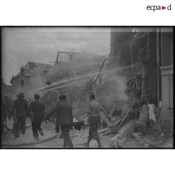 Des volontaires de la défense passive éteignent des ruines fumantes après un bombardement allemand dans un village