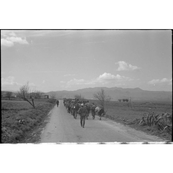 En Crète, dans le secteur de Maleme, une colonne de prisonniers italiens progresse sous la garde d'une sentinelle allemande.
