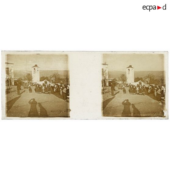 [Vie locale : groupe de femmes sur la place d'un village, ombre du photographe au premier plan].<br>