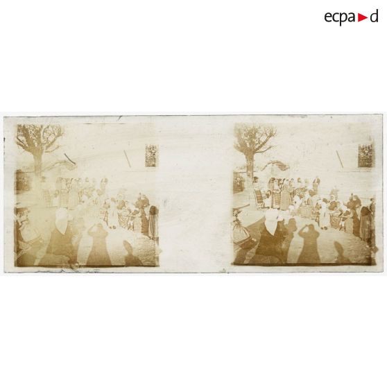 [Vie locale : groupe de femmes sur la place d'un village, ombre du photographe au premier plan].<br>