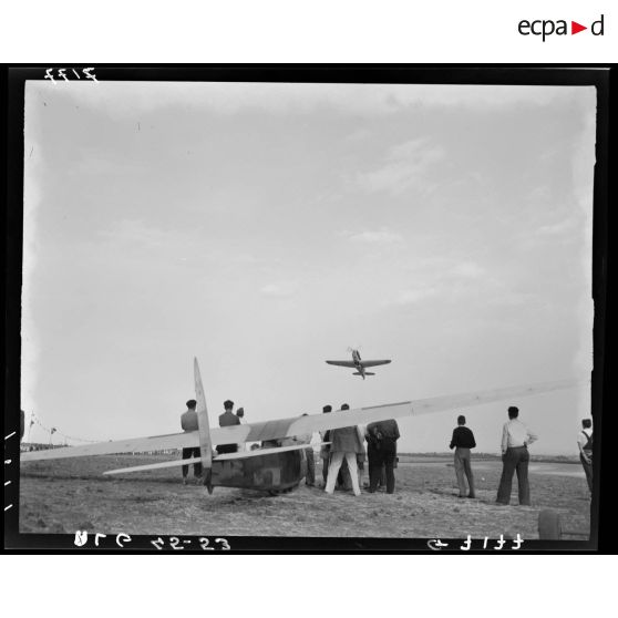 Un avion de transport en plein vol, sous le regard de spectateurs rassemblés autour d'un planeur.