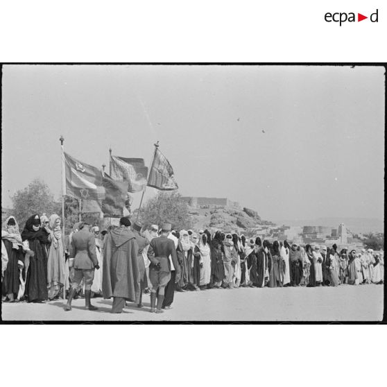 Le général de corps d'armée Henry Martin, commandant le 19e corps d'armée (CA), est accueilli par la population Touareg, à Ghât ; laquelle arbore des drapeaux.