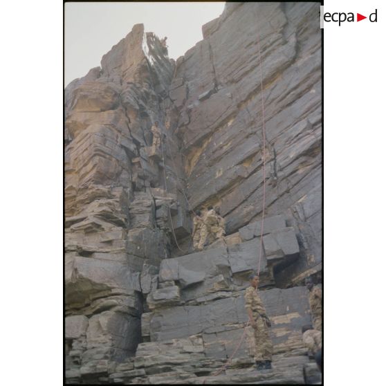 Formation des aides moniteurs commando et des élèves officiers de l'école militaire interarmes d'Atar à l'escalade et au rappel, aux techniques de cordes et d'assurance, au franchissement de fortune, au brancardage dans les falaises de l'Oued Illïj, région d'Atar et d'Azougui. Température d'exercice avoisisant les 40° en raison du rayonnement sur les parois rocheuses, 300 élèves et 10 aides moniteurs ont été formés pendant cette période. [légende d'origine]<br>