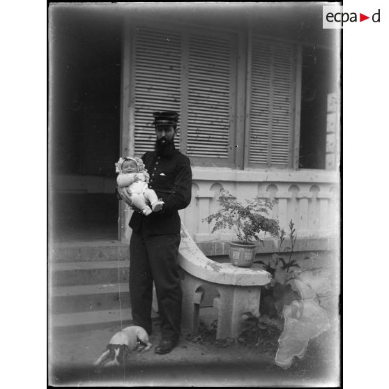 [Papa en uniforme de capitaine tenant bébé devant la maison].<br>
