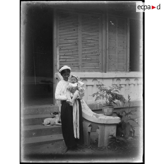 [Le bébé avec une nourrice vietnamienne devant la maison].