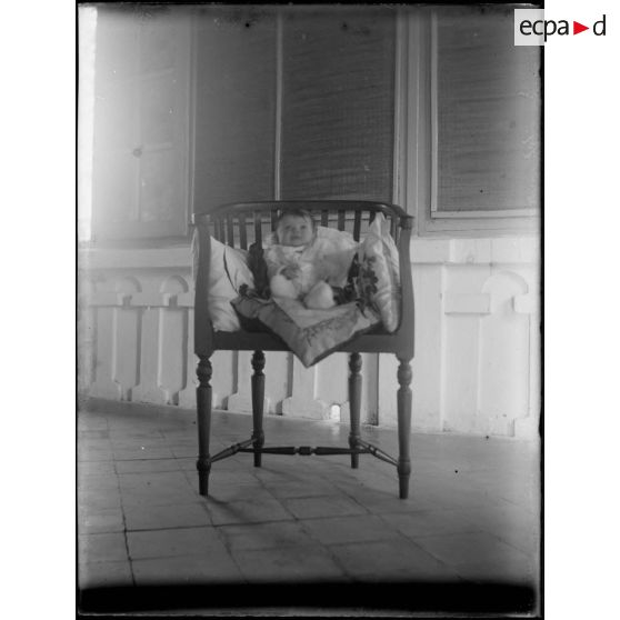 [Portrait de bébé installé dans une chaise garnie de coussins].<br>
