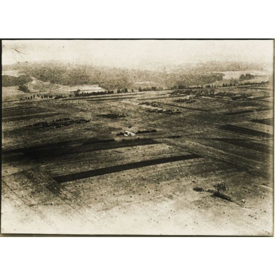 [Photographie aérienne d'un avion survolant une armée en marche dans une plaine].