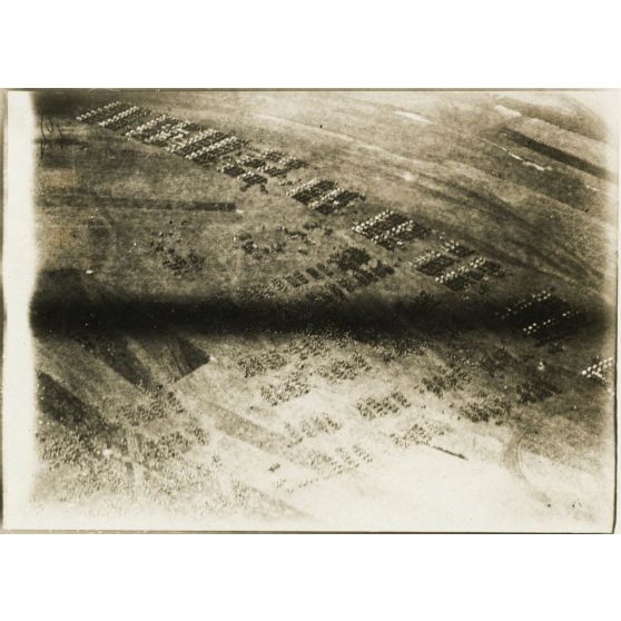 [Photographie aérienne d'un avion survolant une armée en marche dans une plaine].