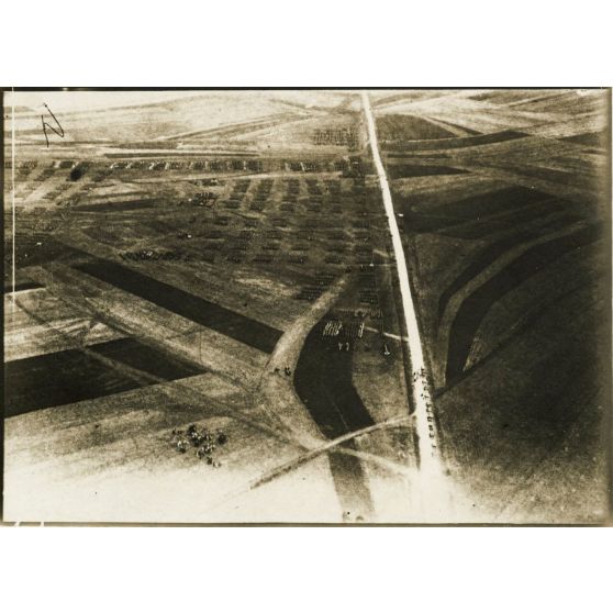 [Photographie aérienne d'un avion survolant une armée en marche dans une plaine].