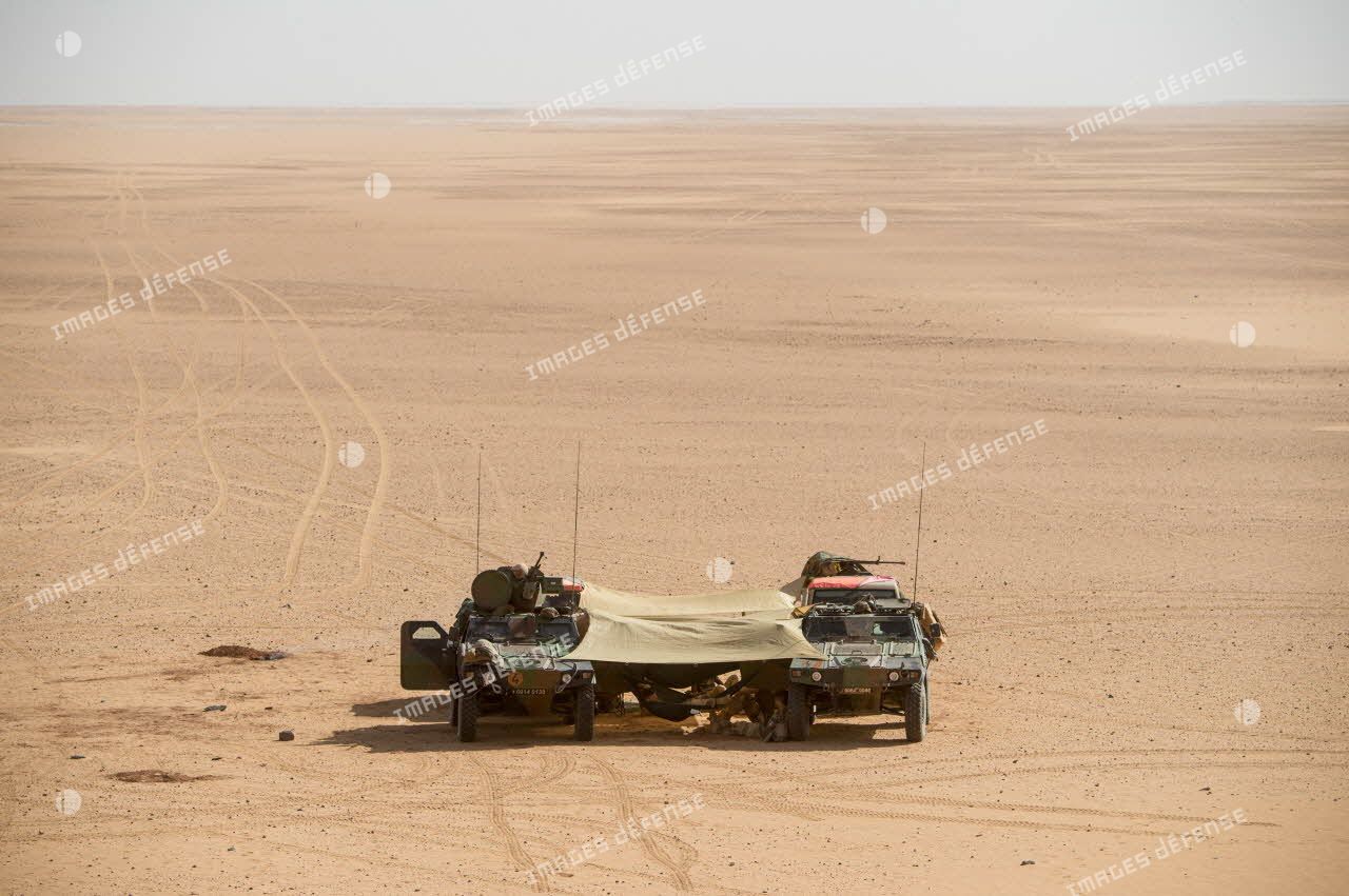 Des soldats d’une patrouille franco-nigérienne se reposent sur des hamacs tendus entre deux véhicules blindés légers (VBL) dans le désert nigérien.