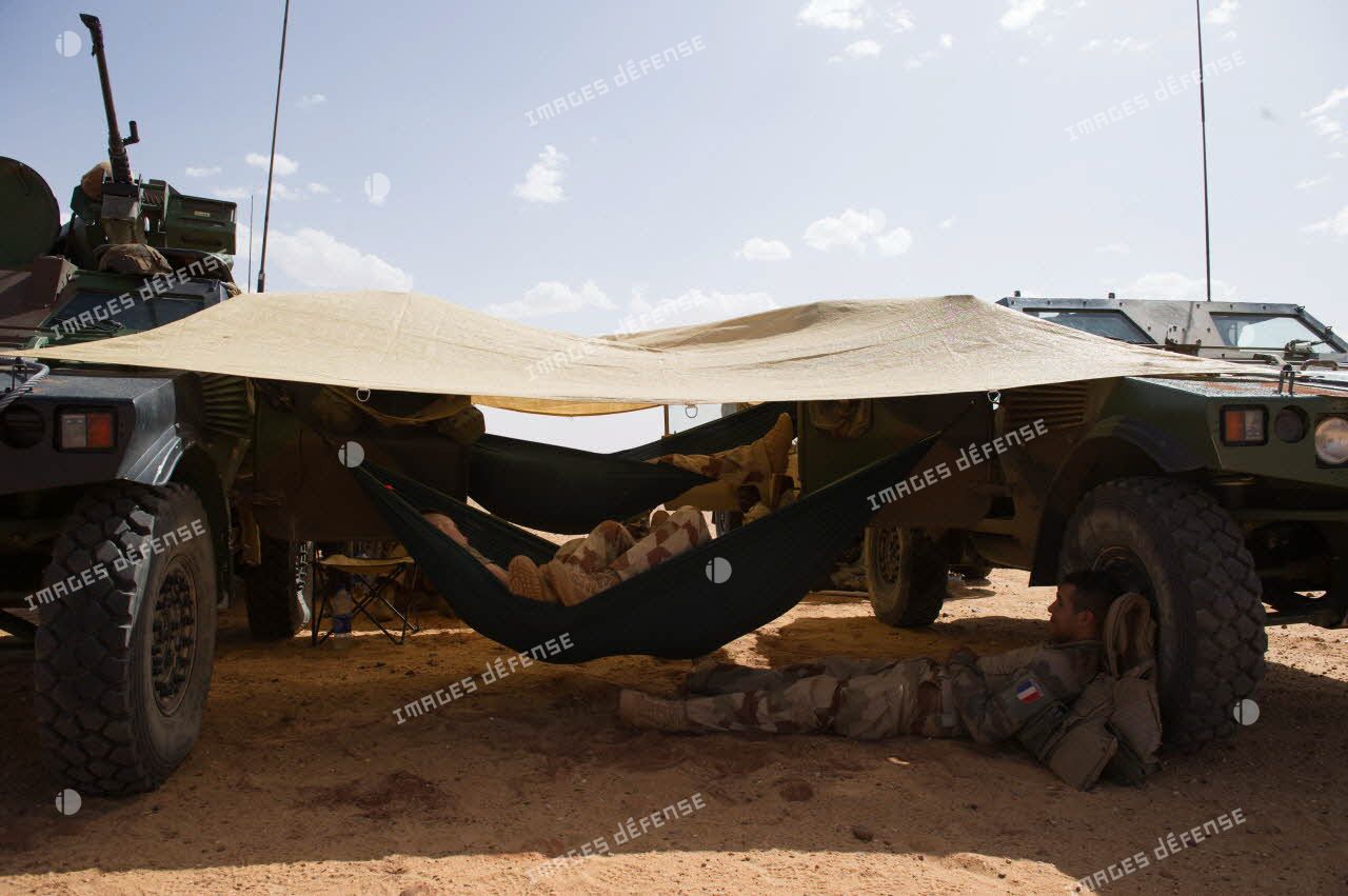 Des soldats d’une patrouille franco-nigérienne se reposent sur des hamacs tendus entre deux véhicules blindés légers (VBL) dans le désert nigérien.