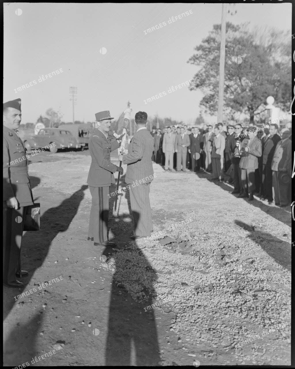 Le général Philippe Leclerc échange un drapeau avec une autorité civile, sous le regard d'autorités civiles et militaires.
