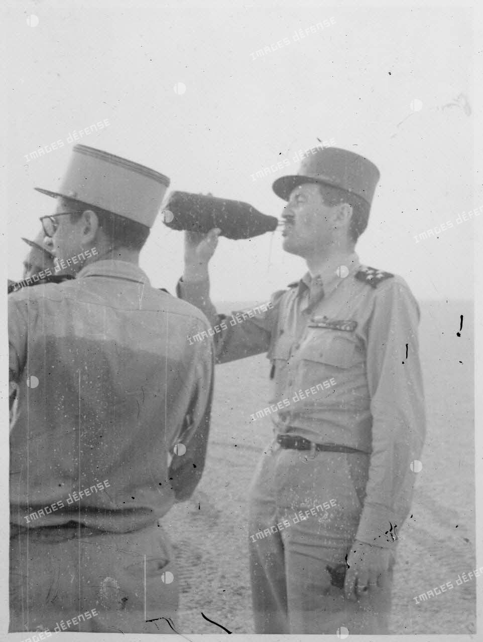 Photographie de profil du général Philippe Leclerc qui se désaltère, dans une région désertique.