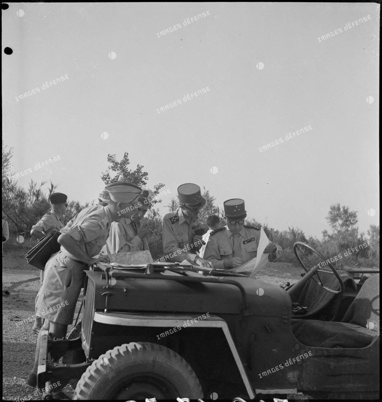 Le général Philippe Leclerc consulte une carte sur le capot d'un véhicule militaire, assisté d'autorités militaires.