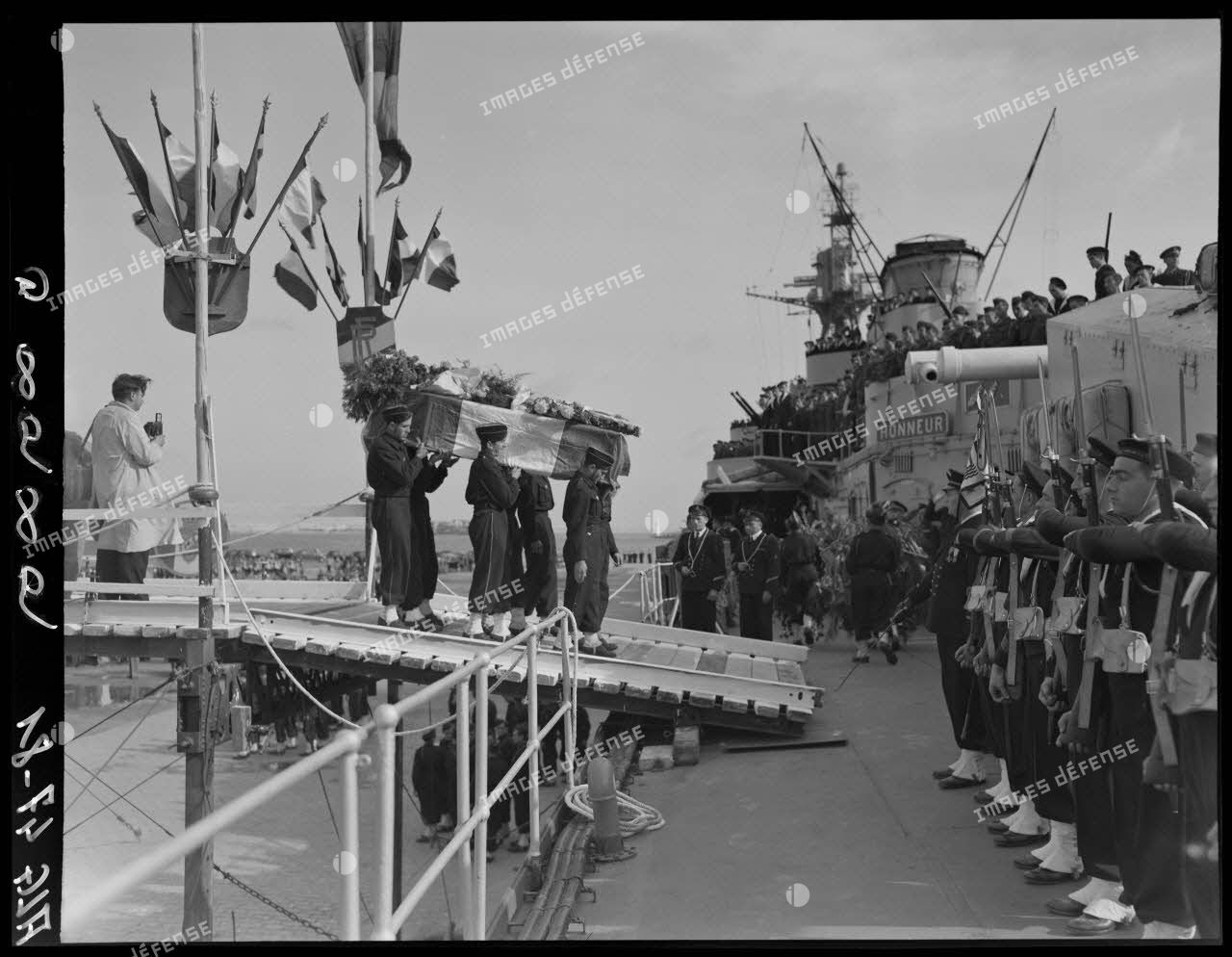 Des soldats transportent les cercueils du général Philippe Leclerc et de ses compagnons, à bord d'un croiseur, à quai, sur le port d'Alger.