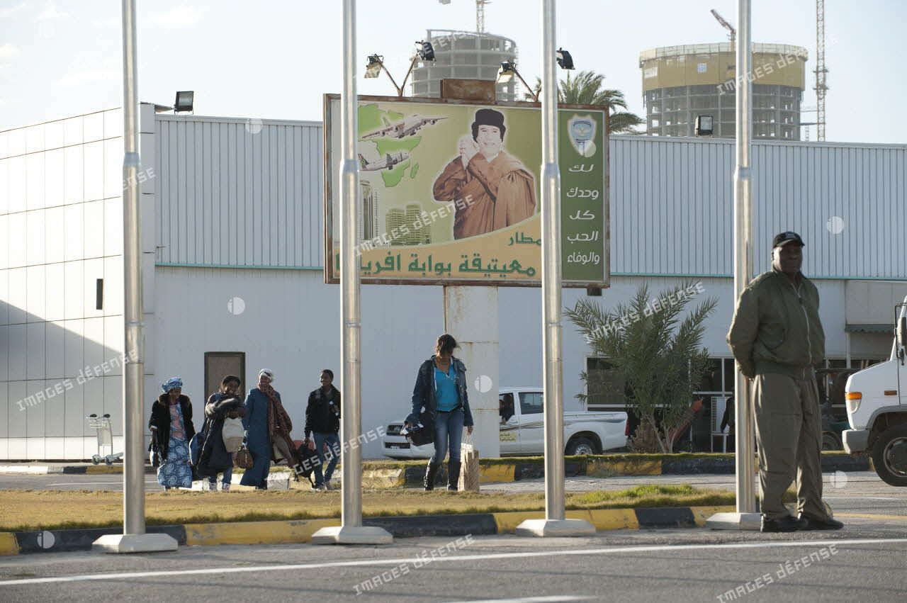 Des ressortissants évacués se dirigent vers leur avion pour l'embarquement sur l'aéroport de Tripoli (Libye), passant près d'une affiche représentant le colonel Kadhafi.