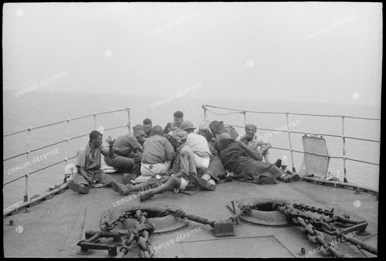 Des tirailleurs du 1er régiment de tirailleurs marocains (RTM) se restaurent sur le pont avant d'un torpilleur ou contre-torpilleur naviguant vers la Corse.
