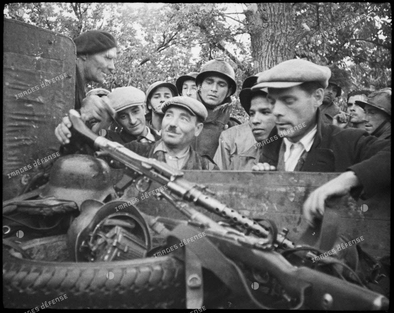 Des partisans corses examinent du matériel abandonné par les Allemands et entreposé dans un camion : des casques, une mitrailleuse MG-34 et son chargeur circulaire.