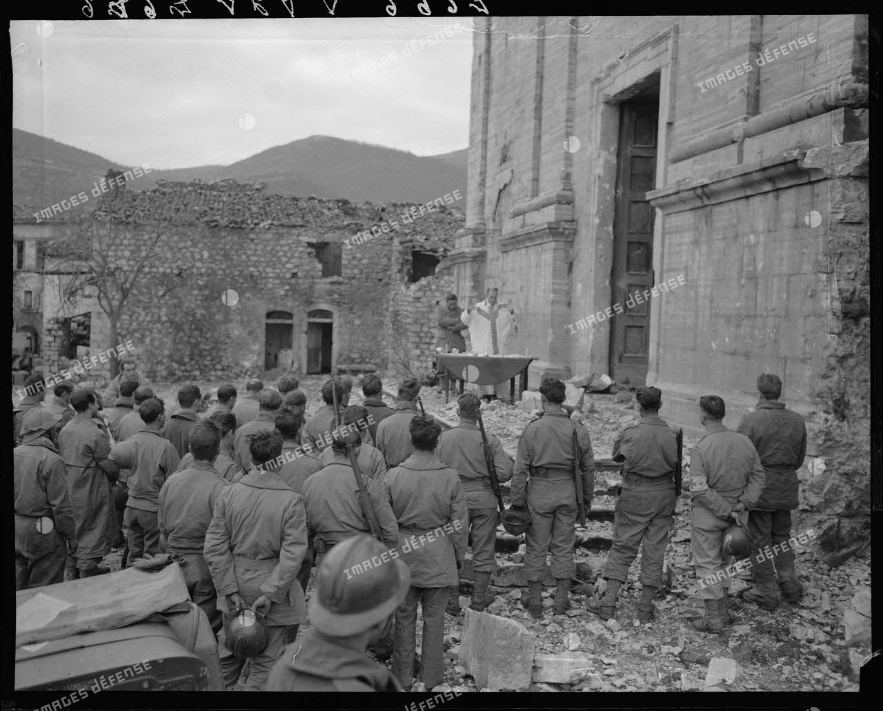 Des tirailleurs du 5e régiment de tirailleurs marocains (RTM) de la 2e division d'infanterie marocaine (DIM) assistent à la messe de Noël, célébrée par un aumônier militaire catholique sur le parvis de l'église d'un village situé à proximité des premières lignes italiennes.