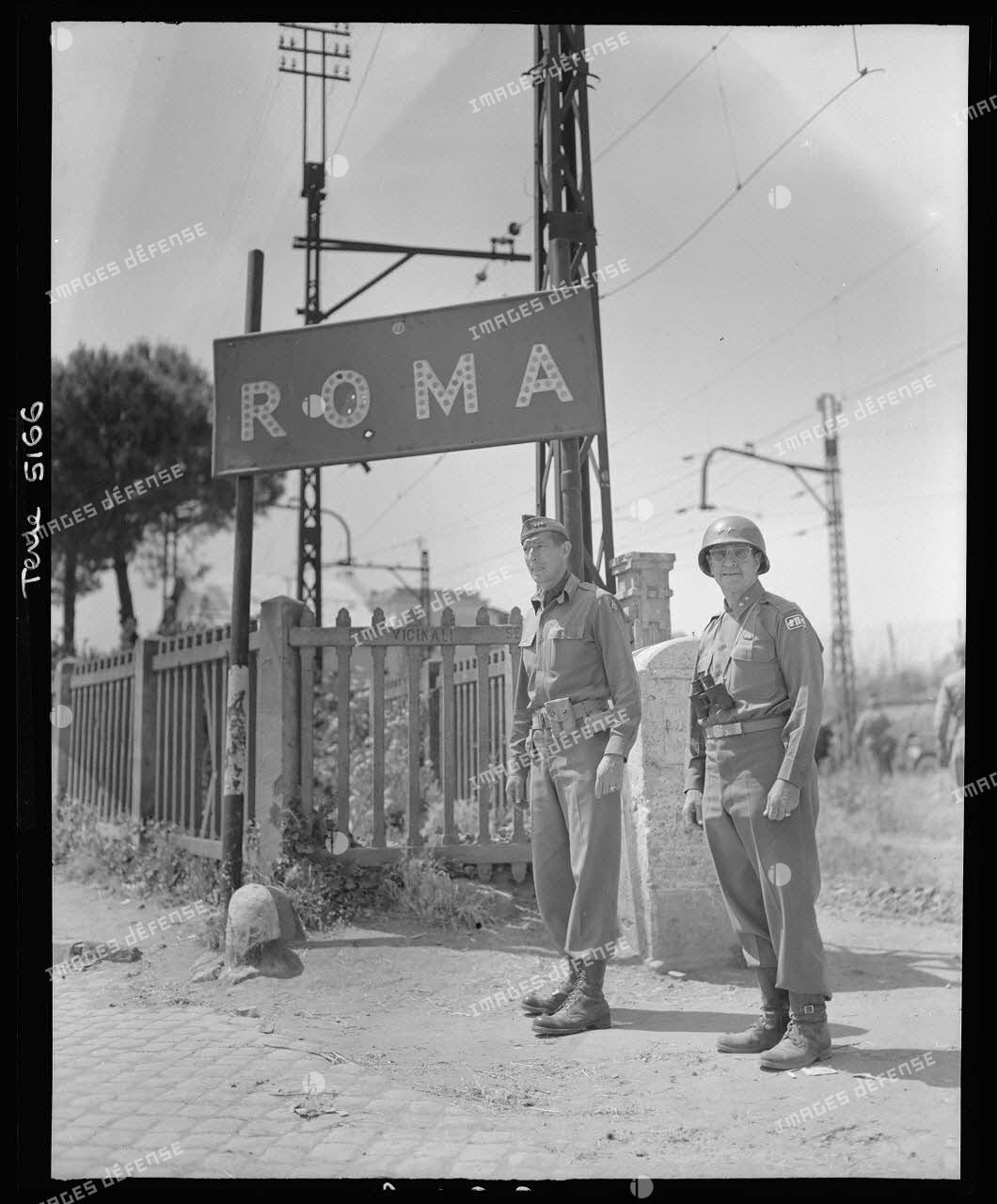 Le lieutenant general Mark Wayne Clark, commandant la 5e armée américaine, pose symboliquement devant un panneau indicateur aux portes de Rome libérée ; à ses côtés, l'un de ses grands subordonnés, le major general Geoffrey Keyes, commandant le 2e corps d'armée.