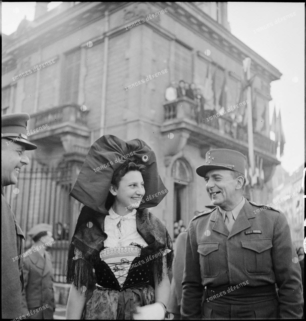 Le général de Lattre de Tassigny pose auprès d'une Alsacienne en costume traditionnel lors d'une cérémonie célébrant la libération de Belfort par les troupes de la 1re armée.