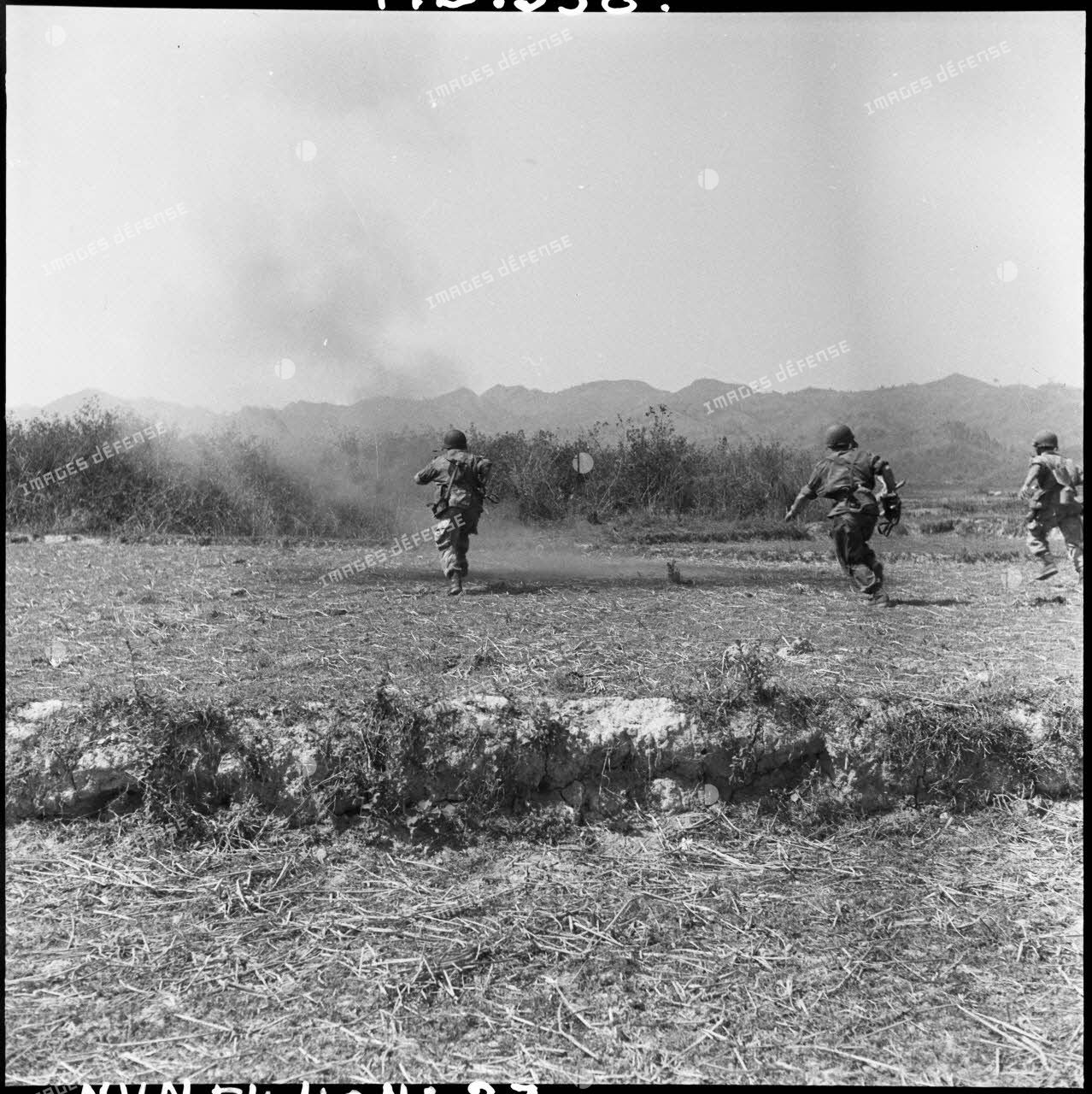 Peu après un tir ennemi, des parachutistes partent à l'assaut de la position Viêt-minh, qui occupe les crêtes à l'arrière-plan.