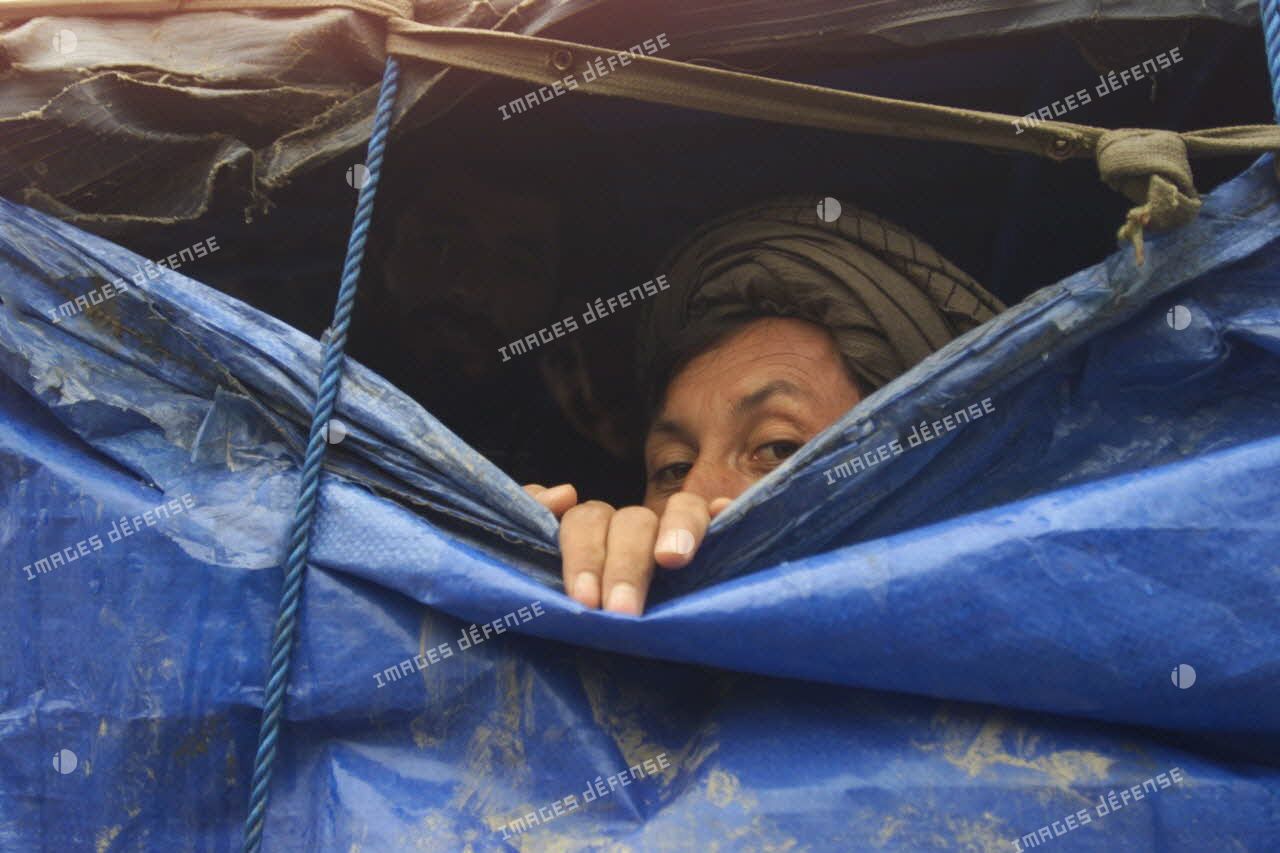 Camp de réfugiés afghans à Mazar e Charif. Les abris du camp sont fabriqués avec des matériaux de récupération pour lutter contre le froid et la pluie. Deux hommes s'abritent derrière des bâches.